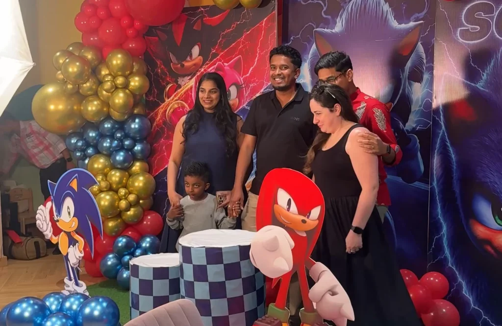 Family celebrating a child's birthday beside Sonic character decorations and balloons